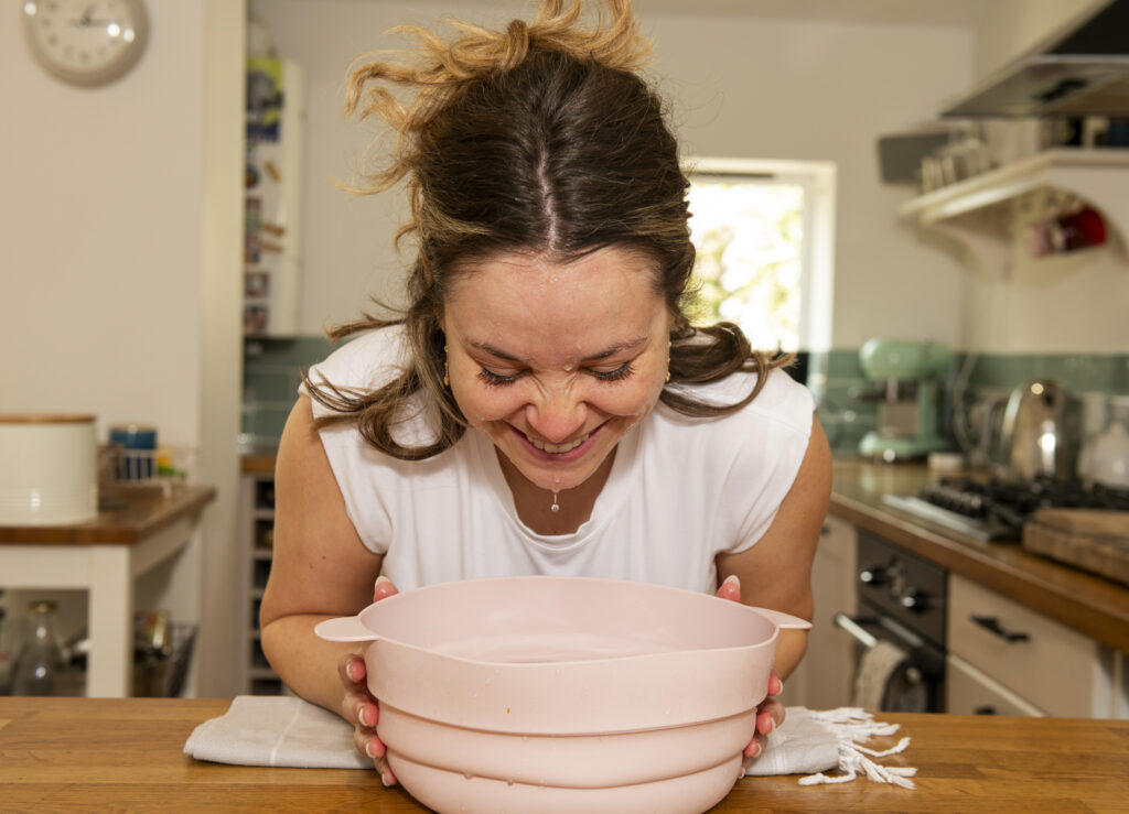 Woman bring head out of FaceDip bowl with water dripping